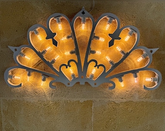 May include: A white metal fan-shaped light fixture with a decorative design. The fixture has multiple light bulbs that are lit and glowing.
