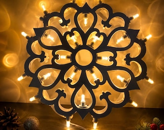 May include: A circular dark-colored decorative frame featuring an intricate cutout pattern of symmetrical floral-like shapes. The frame is illuminated by a series of small, warm-toned LED lights positioned within the cutouts and along the outer edge.