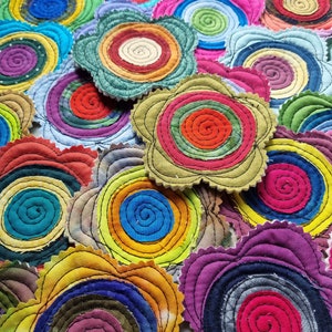 K&ouml;nnte beinhalten: Eine Sammlung bunter Stoffuntersetzer mit Spiraldesign. Jeder Untersetzer besteht aus mehreren Stoffschichten, die ein einzigartiges und strukturiertes Aussehen erzeugen. Die Untersetzer sind perfekt, um jedem Zuhause einen Hauch von handgemachtem Charme zu verleihen.