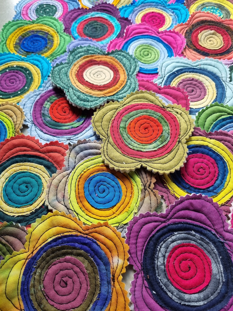 K&ouml;nnte beinhalten: Eine Sammlung bunter Stoffuntersetzer mit Spiraldesign. Jeder Untersetzer besteht aus mehreren Stoffschichten, die ein einzigartiges und strukturiertes Aussehen erzeugen. Die Untersetzer sind perfekt, um jedem Zuhause einen Hauch von handgemachtem Charme zu verleihen.