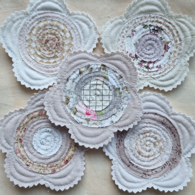 Puede incluir: Cinco posavasos de tela blanca con un dise&ntilde;o circular en tonos beige, marr&oacute;n y gris. Los posavasos est&aacute;n hechos de tela en capas y tienen un borde festoneado.