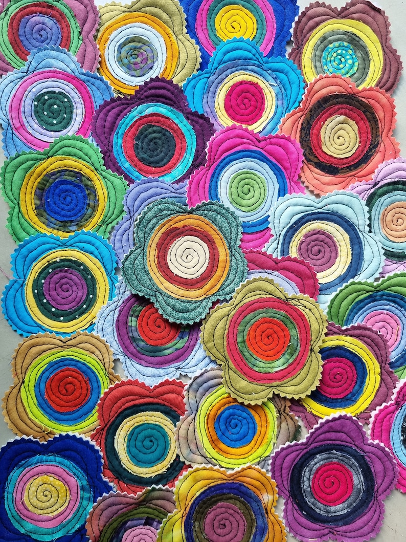 K&ouml;nnte beinhalten: Eine Sammlung von bunten Stoffkreisen mit einem Spiralmuster. Jeder Kreis besteht aus verschiedenen Stoffen und Farben und erzeugt ein lebendiges und einzigartiges Muster.