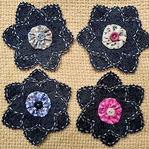 May include: Four denim flower coasters with white stitching and fabric centres. Each coaster features a different centre: floral print with a grey button, floral print with a pink button, blue floral print with a black button, and pink floral print with a white button.