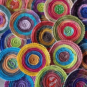 May include: A collection of colorful, circular fabric coasters with a spiral design. The coasters are made of different fabrics and colors, including red, blue, green, yellow, and orange.