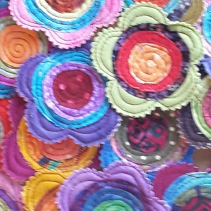 K&ouml;nnte beinhalten: Eine Sammlung bunter Stoffblumen mit mehreren Stofflagen in Blaut&ouml;nen, Rot, Orange, Gr&uuml;n und Lila. Die Blumen sind zusammengen&auml;ht und haben einen einzigartigen, handgefertigten Look.