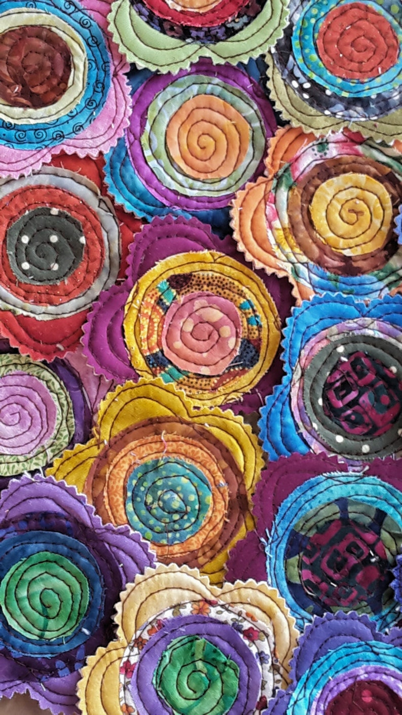 K&ouml;nnte beinhalten: Eine Sammlung von bunten Stoffkreisen mit einem Spiralmuster. Jeder Kreis besteht aus mehreren Stoffschichten, die ein strukturiertes und dreidimensionales Aussehen erzeugen. Die Kreise sind in einem zuf&auml;lligen Muster angeordnet, wodurch ein optisch ansprechendes und einzigartiges Design entsteht.