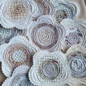 Puede incluir: Una colecci&oacute;n de posavasos de tela hechos a mano con una variedad de patrones y colores. Los posavasos son circulares y tienen un borde festoneado. Los patrones incluyen espirales, dise&ntilde;os florales y formas geom&eacute;tricas. Los colores son principalmente beige, marr&oacute;n y blanco.