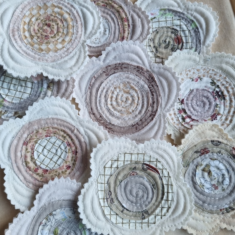 Puede incluir: Una colecci&oacute;n de posavasos de tela hechos a mano con una variedad de patrones y colores. Los posavasos son circulares y tienen un borde festoneado. Los patrones incluyen espirales, dise&ntilde;os florales y formas geom&eacute;tricas. Los colores son principalmente beige, marr&oacute;n y blanco.