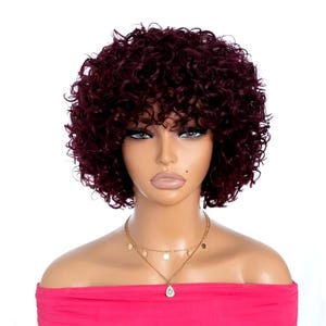 Peut inclure: Une perruque courte et bouclée de couleur bordeaux avec une raie sur le côté et une frange. La perruque est sur une tête de mannequin.