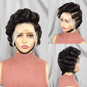 Peut inclure: Une perruque courte noire avec une texture ondulée. La perruque est coiffée en coupe courte avec une raie sur le côté. La perruque est sur une tête de mannequin portant une chemise rose.