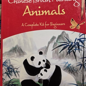 May include: A red instructional book titled Learn the Art of Chinese Brush Painting Animals: A Complete Kit for Beginners. The cover features a painting of two pandas in a bamboo forest with mountains and a waterfall, plus a butterfly and brush.