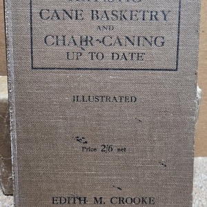 May include: A vintage book titled "Artistic Cane Basketry and Chair-Caning Up To Date" by Edith M. Crooke. The cover is a muted brown with black text, including "Illustrated" and a price. The book's age is evident in its well-worn condition.