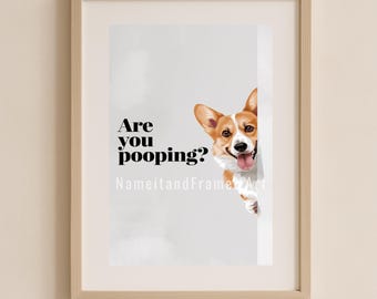 May include: A framed print featuring a cartoon illustration of a corgi dog peeking out from behind a white wall with the text "Are you pooping?" printed below the dog.