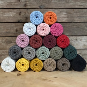 Puede incluir: Una pirámide de 20 madejas de hilo de colores en varios tonos de azul, rosa, rojo, verde, gris, marrón y amarillo. Las madejas están dispuestas en forma de triángulo, con la madeja más grande en la parte inferior y la más pequeña en la parte superior.