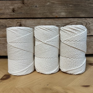 Puede incluir: Tres carretes de cuerda de algodón blanco natural, cada uno enrollado en espiral. La cuerda es gruesa y texturizada, perfecta para manualidades.