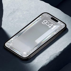 May include: A black smartphone with a clear, bejeweled screen protector. The screen displays the time, 9:41, and the date, Monday, June 6. The phone is set against a textured, light gray surface with dark shadows.