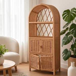 Puede incluir: Una estantería alta de mimbre color marrón claro con parte superior arqueada, que presenta una sección abierta con diseño de celosía en el respaldo y dos armarios inferiores con puertas dobles. Hecha de ratán tejido natural.