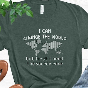 May include: Dark green t-shirt with the text "I CAN CHANGE THE WORLD but first I need the source code" and a world map graphic. The shirt is paired with blue jeans and brown sandals.