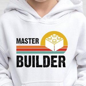 May include: White hooded sweatshirt with a front pocket and the words "MASTER BUILDER" in black. The design includes a yellow sun with a white and yellow building block, and horizontal stripes in red, orange, and teal.