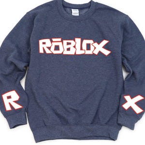 May include: A navy blue sweatshirt with the word "ROBLOX" in white letters with red outlines across the chest. The letter "R" is on the left sleeve and the letter "X" is on the right sleeve, both in white with red outlines.