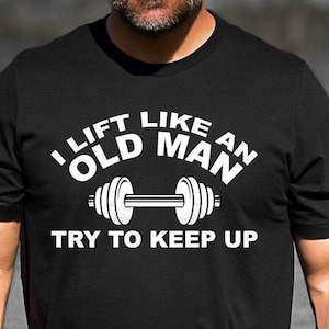 May include: A black t-shirt with white text that reads 'I lift like an old man try to keep up' and a white image of a dumbbell.