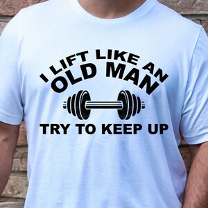 Peut inclure: T-shirt blanc avec l'inscription noire "I LIFT LIKE AN OLD MAN TRY TO KEEP UP" et un halt&egrave;re. Le t-shirt est &agrave; col rond.