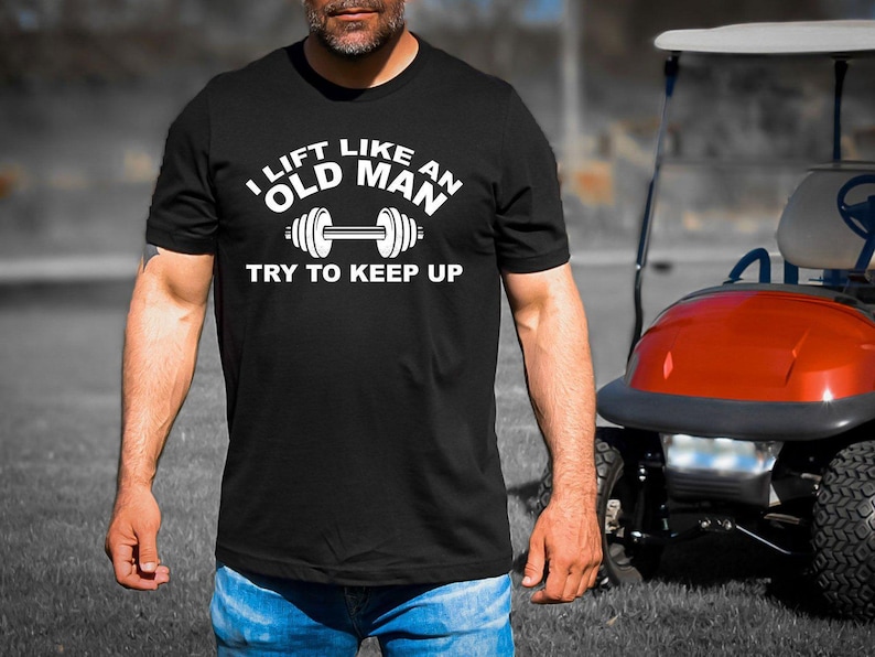 May include: A black t-shirt with white text that reads 'I lift like an old man try to keep up' and a white image of a dumbbell.