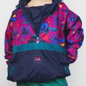 以下が含まれることがあります： マゼンタ、青、黄色の鮮やかな模様のヴィンテージアノラックジャケット。 ジャケットは、ターコイズのストライプと「Exile Jeantex」のロゴが付いたネイビーブルーの下部セクションを備えています。 ジッパーフロントとハイカラーが特徴です。