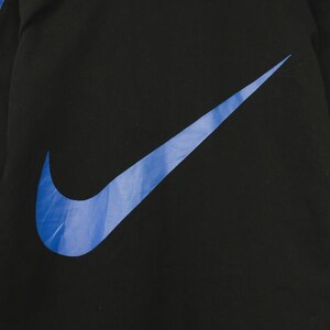 Op de afbeelding: Zwart sportjack met een groot blauw Nike swoosh-logo op de voorkant. De jas heeft blauwe accenten langs de mouwen. Het Nike-logo is effen blauw.