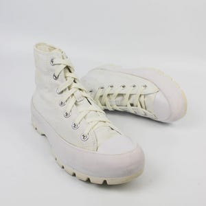 May include: Off-white high-top sneakers with thick, textured soles. The canvas shoes have matching laces and a rubber toe cap. The sneakers are set against a white background.