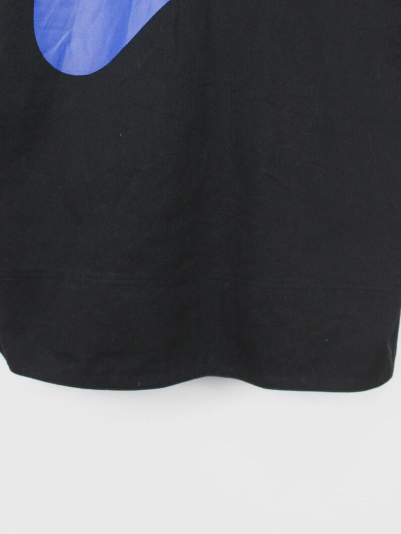 Op de afbeelding: Zwart sweatshirt met een groot blauw swoosh-ontwerp aan de linkerbovenkant. Het sweatshirt is gemaakt van een zacht materiaal en heeft een geribbelde zoom. De achtergrond is effen wit.