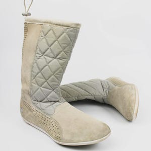 Könnte beinhalten: Hellgraue und beige Winterstiefel. Die Stiefel haben einen gesteppten oberen Bereich und einen Wildleder-ähnlichen unteren Bereich. Die Stiefel haben eine Zugschlaufe oben und ein perforiertes Design an der Seite. Für kaltes Wetter.