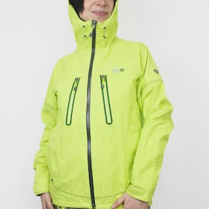 May include: A vibrant lime green hooded jacket with a black zip and green detailing. The jacket features two front pockets with green trim and a logo on the chest. The hood is adjustable, and the jacket is made of a lightweight, waterproof material.