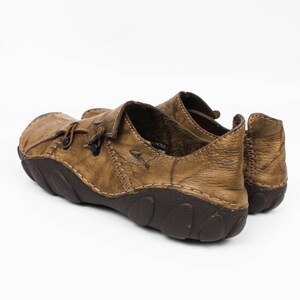 K&ouml;nnte beinhalten: Ein Paar hellbraune Lederschuhe mit Used-Optik, sichtbaren Kontrastn&auml;hten, einer dunkelbraunen, strukturierten Gummisohle und einem Slipper-Design mit einem kleinen seitlichen Riemendetail. Der Markenname Clarks ist seitlich eingepr&auml;gt.