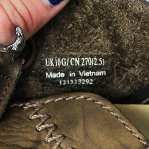 K&ouml;nnte beinhalten: Das Innere eines braunen Lederschuhs mit einem schwarzen Etikett, das den wei&szlig;en Text UK 10G / CN 270(2.5), Made in Vietnam und die Nummer 121313292 tr&auml;gt. Der Schuh hat sichtbare beige N&auml;hte an der Lederkante und ein strukturiertes Innenfutter.