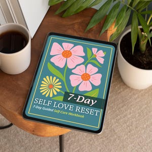 May include: A digital tablet displays a teal floral design with pink flowers and the text "SELF LOVE RESET" and "7-Day Guided Self-Care Workbook." A mug of coffee and a potted plant are in the background.