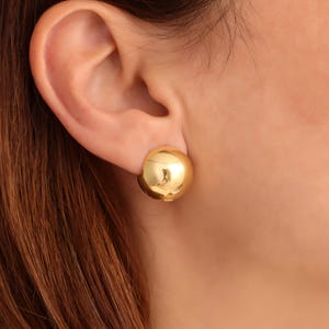 Può includere: Un paio di orecchini a clip dorati con un design rotondo e liscio.