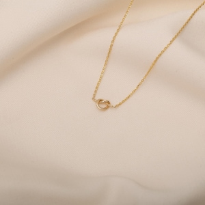 May include: A delicate gold necklace with a simple knot pendant.