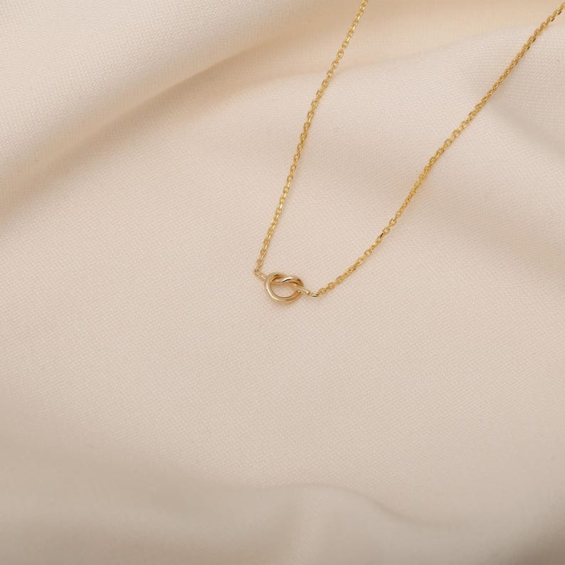 May include: A delicate gold necklace with a simple knot pendant.