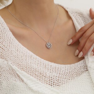 May include: A silver necklace with a small, round pendant featuring a delicate, intricate design of small, clear stones.