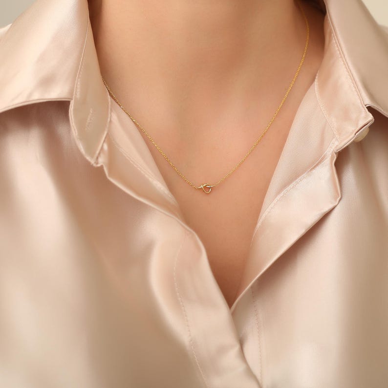 May include: A delicate gold necklace with a simple knot pendant.