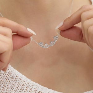 Puede incluir: Un collar de plata con una cadena delicada y un colgante con cinco pequeños diseños en forma de diamante engastados con piedras transparentes.