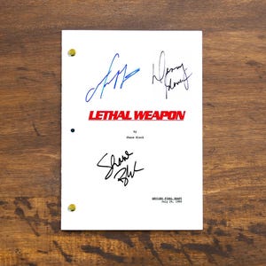 Pode incluir: Uma página de roteiro branca para o filme "Máquina Mortífera" com as assinaturas de Shane Black, Danny Glover e Mel Gibson. A página do roteiro é datada de 28 de julho de 1987.