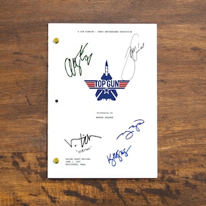 Pode incluir: Uma página de roteiro branca para o filme "Top Gun" com assinaturas dos atores. As assinaturas estão em tinta preta, azul e verde. As assinaturas são de Tom Cruise, Val Kilmer e Anthony Edwards.