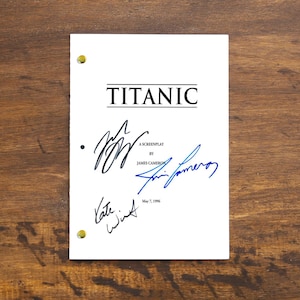 Pode incluir: Um roteiro branco intitulado "TITANIC" com assinaturas em tinta preta e azul. O roteiro é fixado com fixadores de latão e repousa sobre uma superfície de madeira. O texto inclui "A Screenplay by James Cameron" e a data "May 7, 1996."