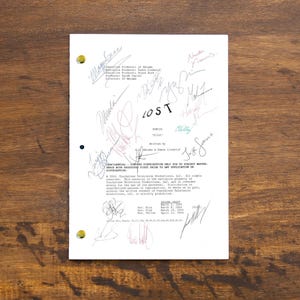 Pode incluir: Uma página de roteiro branca para a série de televisão "LOST" com o título "LOST" escrito em preto no topo. A página é assinada por várias pessoas, incluindo o criador da série, J.J. Abrams. A página também inclui um aviso de direitos autorais.