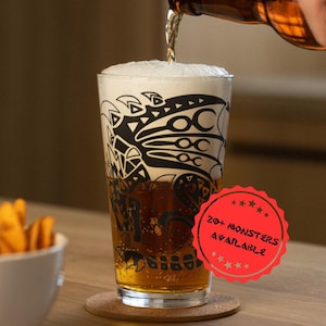 May include: A pint glass with a black monster design is filled with beer as it is poured from a bottle. The glass sits on a coaster. A red sticker reads "20+ MONSTERS AVAILABLE". A bowl of chips is in the background.
