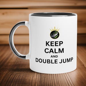May include: White ceramic mug with a black interior and a silver handle. The mug features the text "KEEP CALM AND DOUBLE JUMP" in black, with a gold crown and emblem above the text. The mug is on a wooden surface.