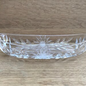 May include: A clear glass oval serving dish with a cut-glass design. The dish has a raised centre and a scalloped edge.