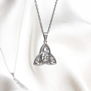 Könnte beinhalten: Silberfarbene Anhängerkette mit einem keltischen Knoten-Design und einem Pentagramm in der Mitte. Der Anhänger hängt an einer filigranen Kette. Die Halskette wird vor einem weißen Hintergrund präsentiert.